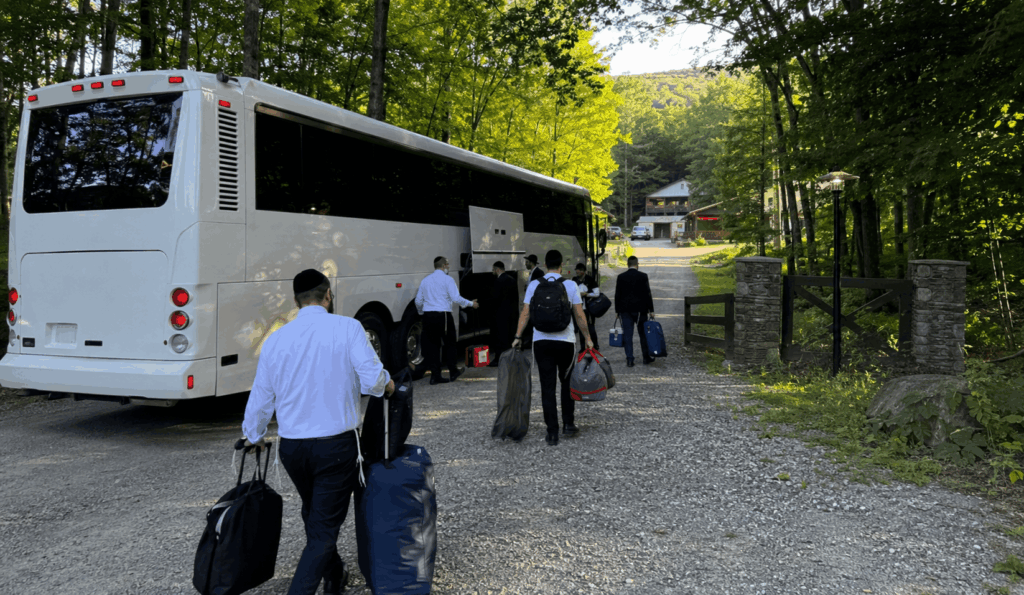 charter bus arriving at a catskills camp property with a community group unloading bags near the main gate