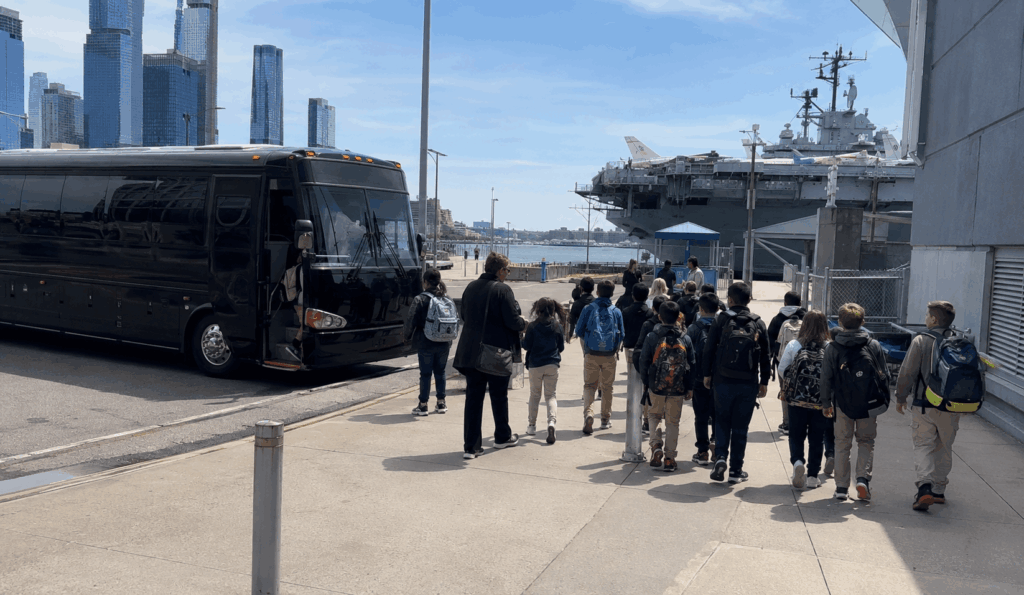 student field trip group with chaperones walking from a charter bus toward the pier 86 entrance at the intrepid museum