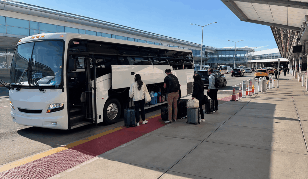 charter bus loading a small group with luggage near a jfk airport terminal curb in queens