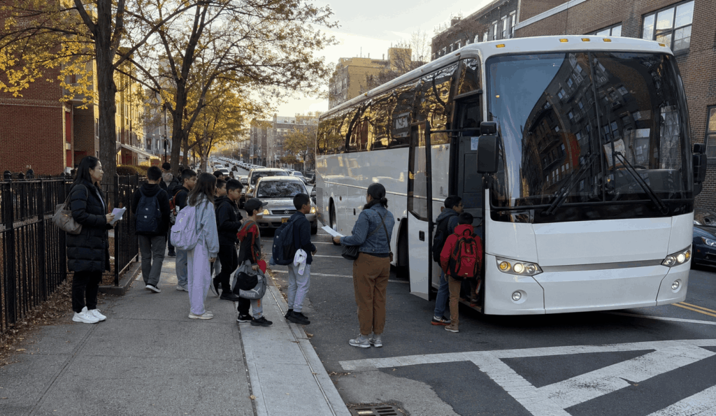 students and chaperones boarding a charter bus outside a queens school before a statue of liberty field trip
